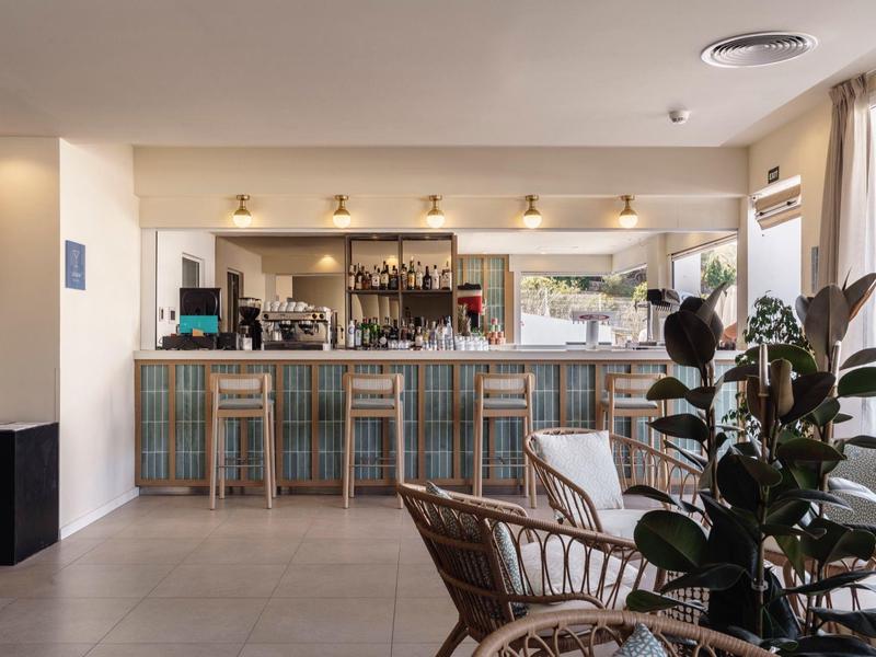 Bar de hotel luminosa con taburetes de madera, plantas en primer plano e iluminación moderna.