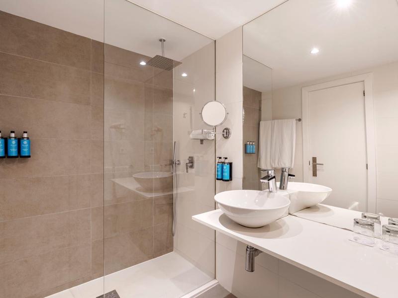 Baño moderno con ducha a ras de suelo, lavabos dobles y espejos grandes.