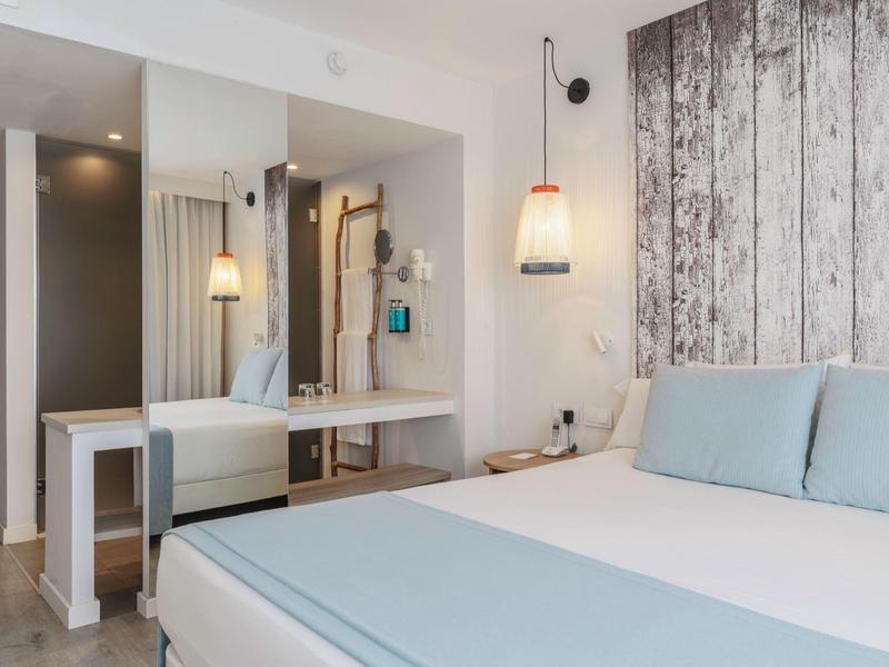 Habitación de hotel moderna con cama grande, cojines azul claro y revestimiento de madera en la pared.