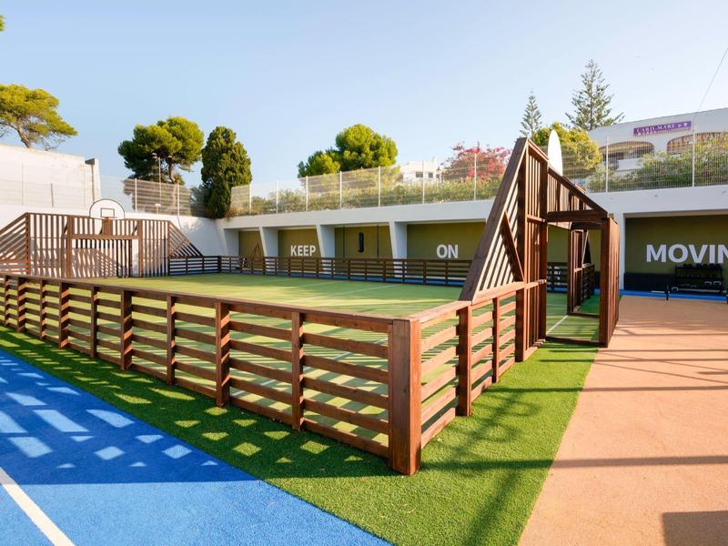 Área exterior moderna con cancha de tenis y elementos de madera junto a pista azul de atletismo.