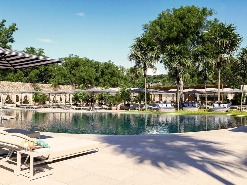 Amplia área de piscina con tumbonas y sombrillas, rodeada de árboles y cielo despejado.