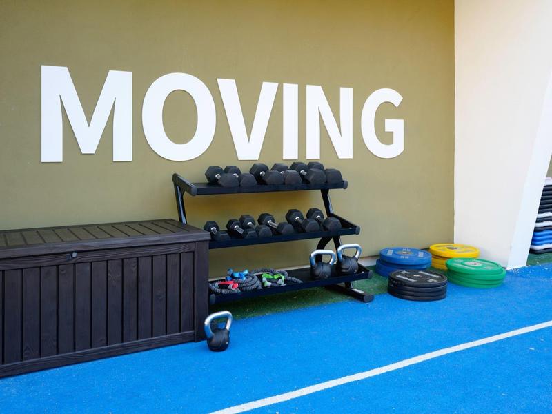 Área de gimnasio con pesas, mancuernas y accesorios en el suelo junto a una pared con la palabra MOVING