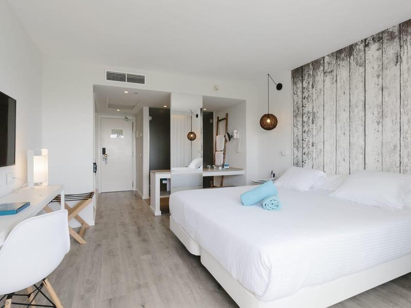 Habitación de hotel luminosa con cama doble, suelo de madera y decoración moderna.