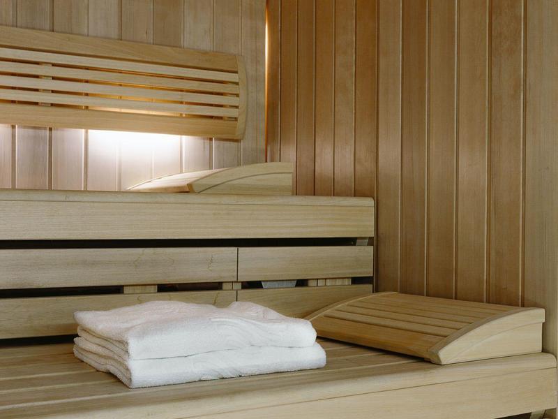 Sauna de madera clara con toallas blancas dobladas y reposacabezas sobre el banco.