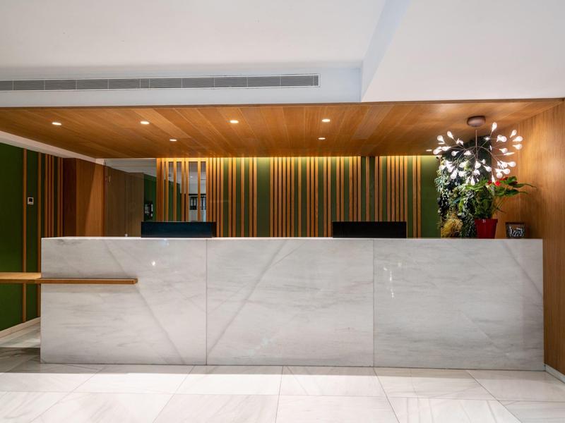 Recepción de hotel moderna con amplio mostrador de mármol blanco y pared colorida al fondo.