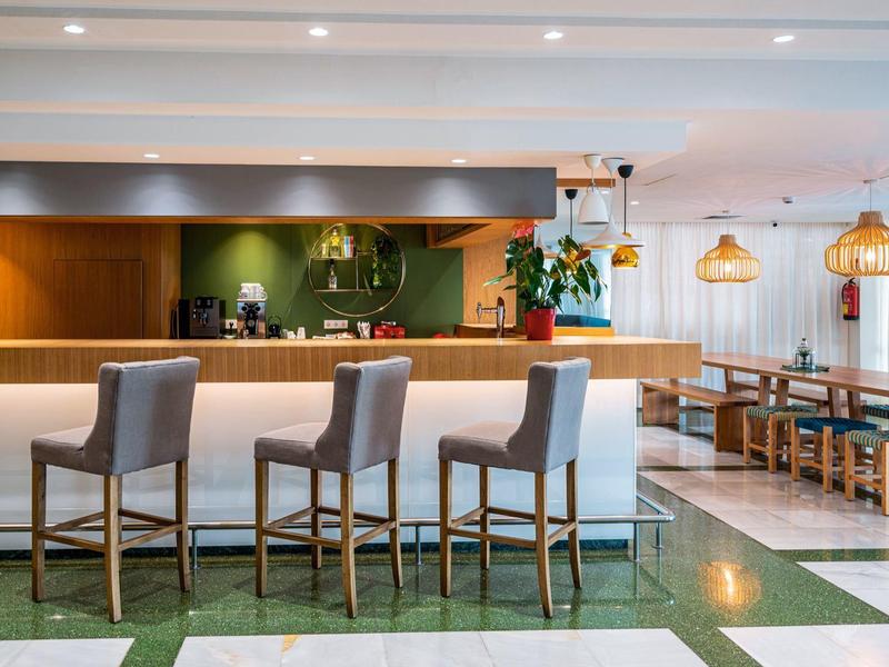 Bar moderno con taburetes altos y área de asientos con mesas y lámparas colgantes en un hotel.