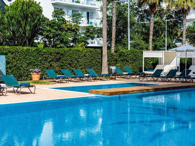 Gran piscina exterior con tumbonas y sombrillas en un día soleado en el hotel.