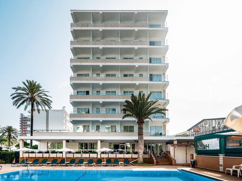 Edificio de hotel moderno con varios balcones y piscina en primer plano bajo cielo despejado.