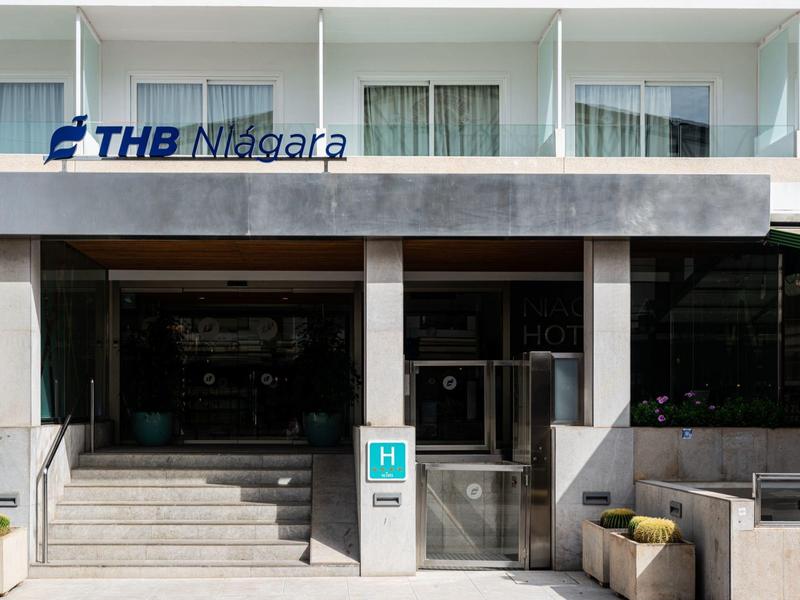 Entrada de un hotel con escaleras, ventanas de vidrio y logo THB Niagara sobre la entrada.