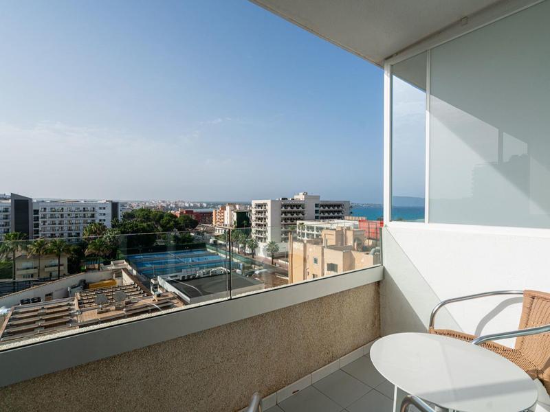 Balcón con silla y mesa con vista a hoteles y el mar en el horizonte.