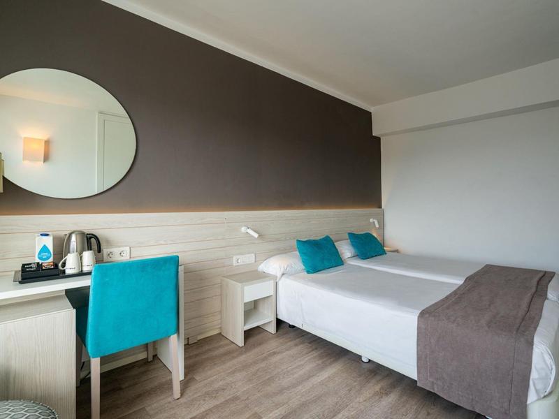 Habitación de hotel moderna con cama doble, escritorio, silla azul y espejo redondo en la pared.