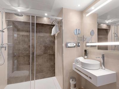 Modernes Badezimmer mit begehbarer Glasdusche und Wandwaschbecken in neutralen Farbtönen.