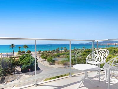 Balkon mit weißen Stühlen und Tisch mit Meerblick und Palmen unter blauem Himmel