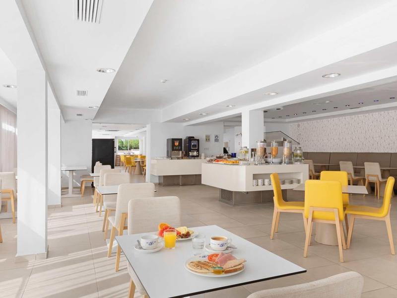 Sala de desayuno moderna con sillas amarillas y mesas servidas en un área luminosa del hotel.