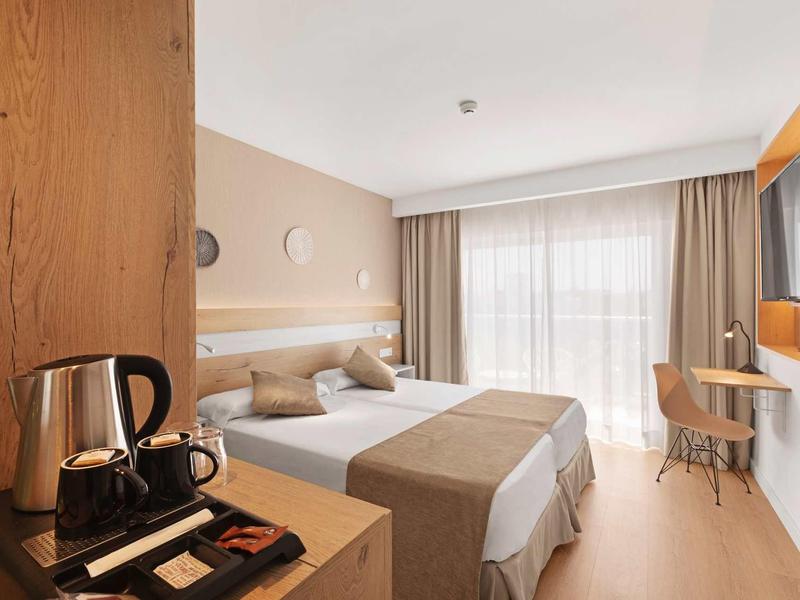 Habitación de hotel moderna con cama doble, cafetera y ventana grande con cortinas.