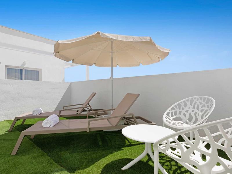 Dos tumbonas con toallas bajo una gran sombrilla en césped junto a casa blanca.