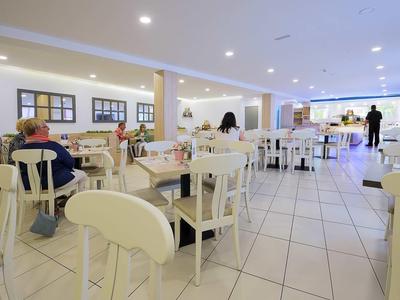 Jasna sala jadalna w hotelu z białymi meblami i kilkoma gośćmi.