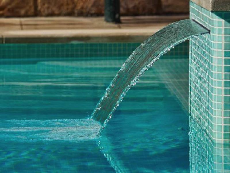 De l'eau claire s'écoule d'une fontaine carrelée de vert dans une piscine.