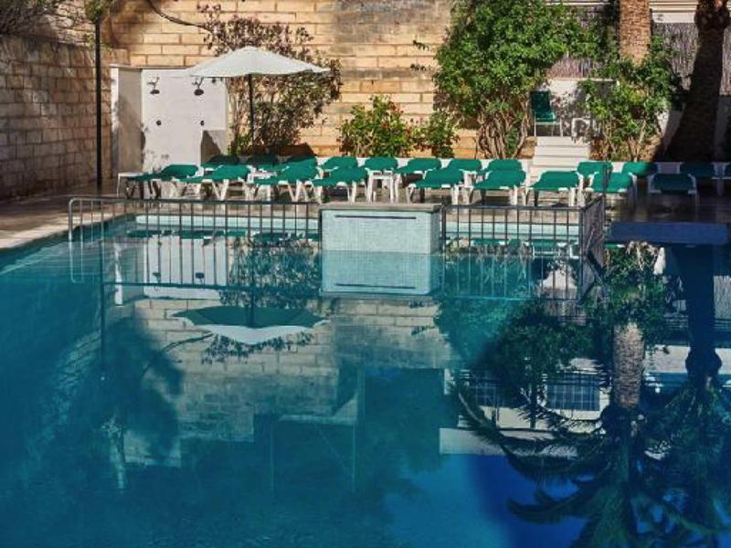 Piscine avec chaises longues et parasol dans une cour ensoleillée avec mur en pierre.