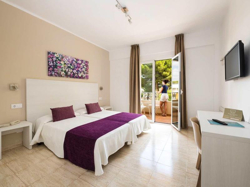 Chambre d'hôtel lumineuse avec lit double, accents violets et accès à une terrasse donnant sur le jardin.