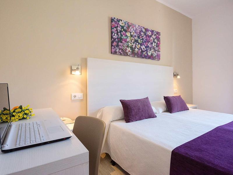 Chambre d'hôtel moderne avec lit double, décor violet et ordinateur portable sur le bureau