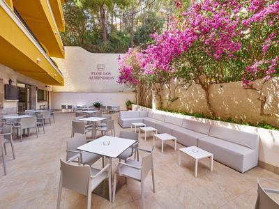 Słoneczny taras hotelowy z stołami, krzesłami i kwitnącą bugenwillą.