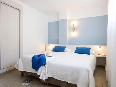 Jasny pokój hotelowy z podwójnym łóżkiem, niebieskimi akcentami i szafą przesuwaną.