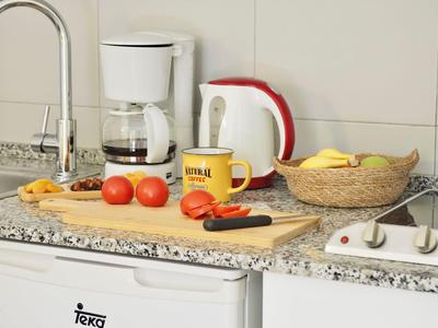 Blat kuchenny z ekspresem do kawy, czajnikiem, koszem na owoce i deską do krojenia z pomidorami.