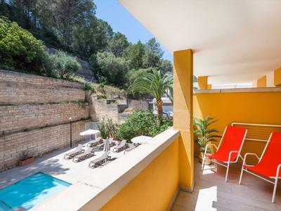 Balkon z pomarańczowymi krzesłami z widokiem na basen i leżaki w ogrodzie.