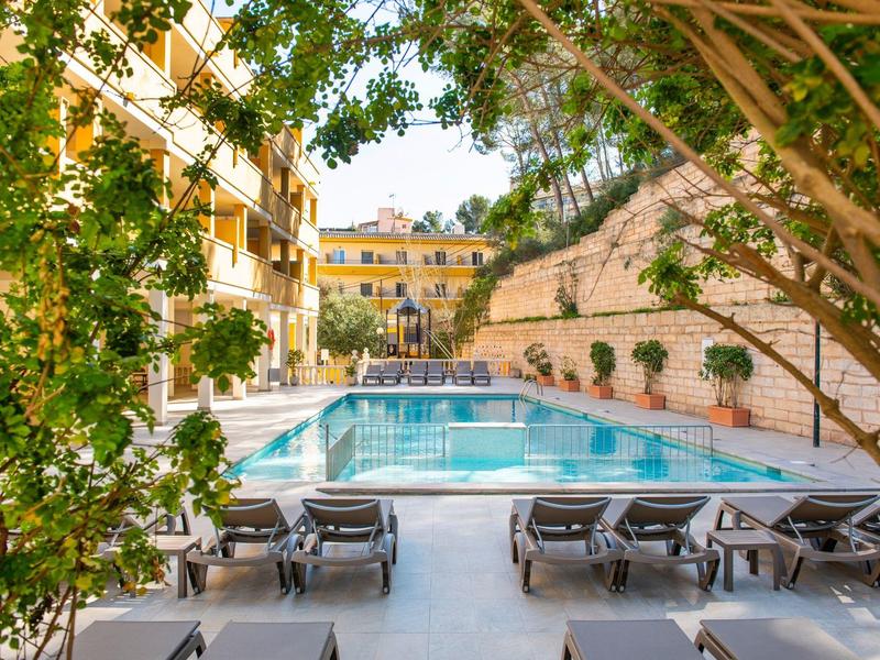 Basen na zewnątrz z leżakami i otaczającymi budynkami, otoczony zielonymi roślinami.