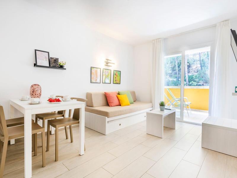 Jasny salon z częścią jadalną, sofą, kolorowymi poduszkami i balkonem z przeszklonymi drzwiami.