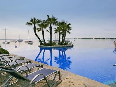 Infinity-Pool mit Palmeninsel und Liegestühlen am Ufer unter klarem Himmel