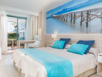 Nowoczesny pokój hotelowy z łóżkiem podwójnym, niebieskimi akcentami i widokiem na morze z balkonu.