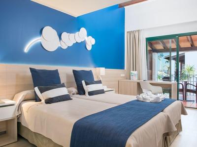 Nowoczesny pokój hotelowy z dwoma łóżkami pojedynczymi, niebieskimi akcentami i dostępem do tarasu.