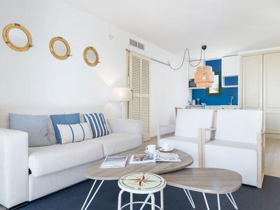 Jasny salon z białą sofą, fotelami, okrągłymi stolikami i marynistycznymi dekoracjami ściennymi.