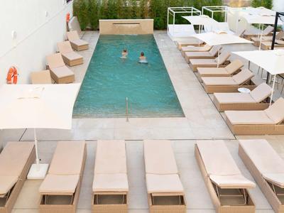 Moderner Pool mit zwei Schwimmern, von Liegestühlen und Sonnenschirmen umgeben, helle Farben.