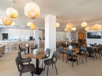 Modernes Restaurant mit runden Tischen, Stühlen und dekorativen Hängelampen in einem hellen Raum.