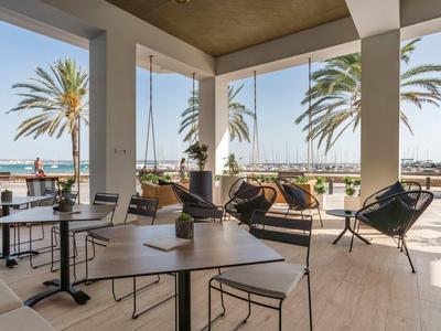 Terrasse eines Hotels mit Esstischen, Stühlen und Blick auf das Meer mit Palmen.