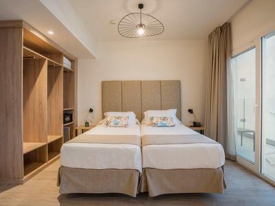 Modernes Hotelzimmer mit zwei Einzelbetten, Holzkleiderschrank und Terrasse mit Glaswand.