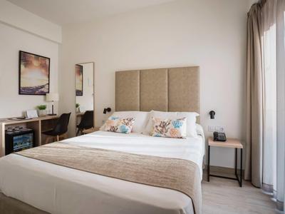 Modernes Schlafzimmer mit großem Bett, Schreibtisch, Stuhl und großem Fenster mit Vorhängen.