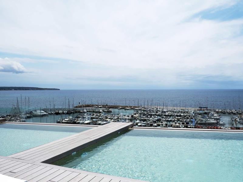 Infinity pool overlooking marina and sea under cloudy sky.