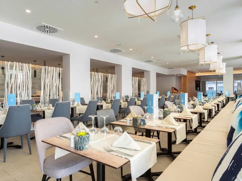 Modern restaurant with light tables, blue chairs, and decorative lighting.