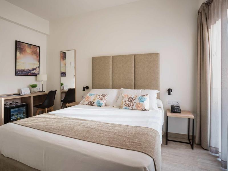 Modern hotel room with large bed, desk, and window with curtains.