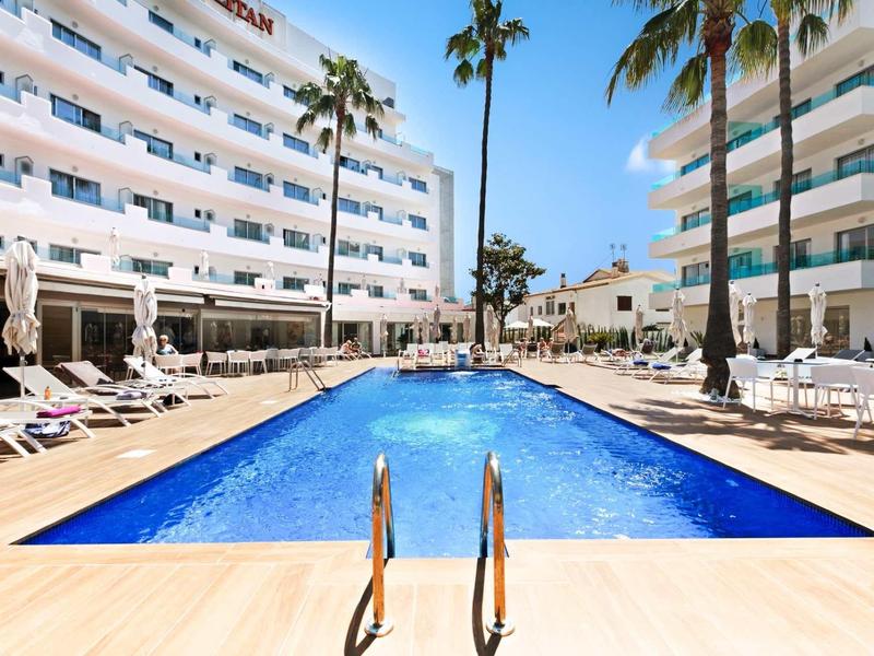 Piscine extérieure moderne entre deux bâtiments d'hôtel avec palmiers et chaises longues.