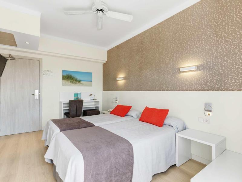 Chambre d'hôtel moderne avec lit double, deux oreillers rouges et éclairage mural.