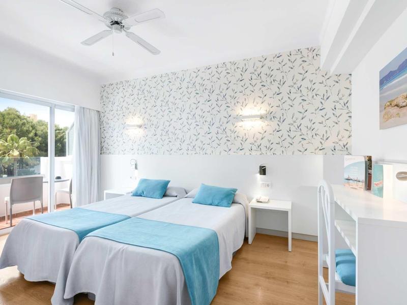 Chambre d'hôtel lumineuse avec deux lits, accents bleus et balcon avec vue sur les arbres.