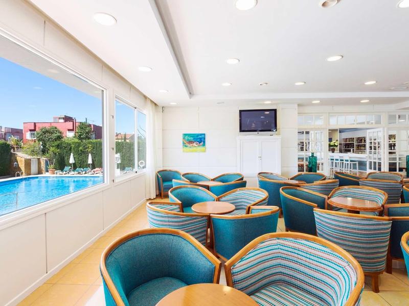 Heller Raum mit blauen Sesseln, runden Holztischen, großen Fenstern und Blick auf Pool und Stadt.