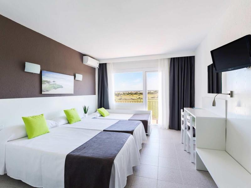 Modernes Hotelzimmer mit drei Betten, weißen Wänden, brauner Akzentwand und Fenster mit Vorhängen.