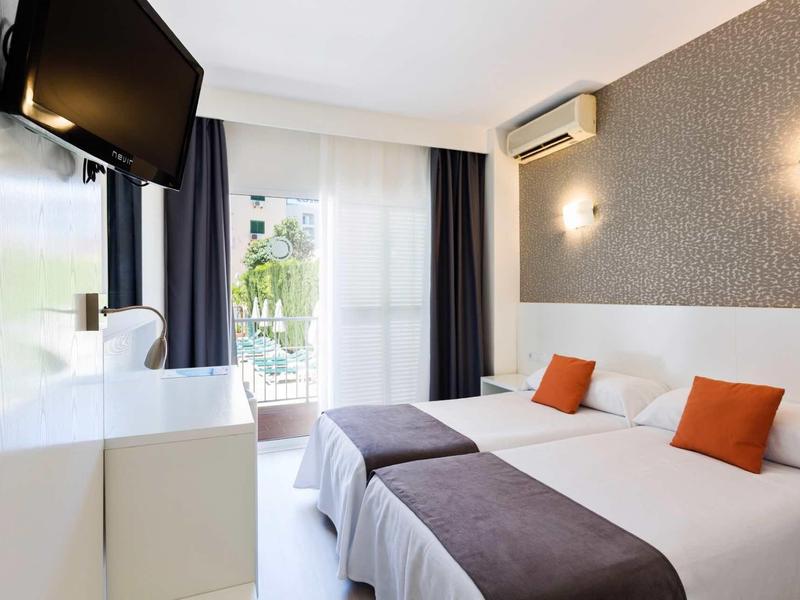 Helles Hotelzimmer mit zwei Einzelbetten, weißen Wänden, grauem Teppich und Balkon mit grünem Ausblick.