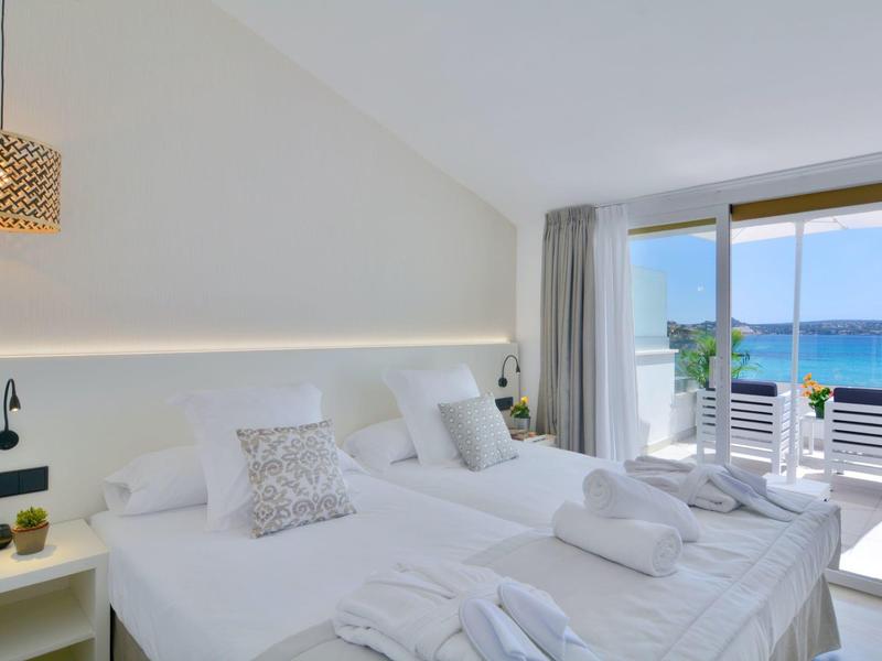 Chambre d'hôtel lumineuse avec deux lits et vue sur la mer par de grandes fenêtres.